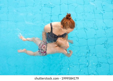 The Child Learns To Swim. Mom And Daughter Are Swimming In The Pool. Top View.