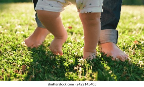 El niño aprende a dar los primeros pasos en la hierba. El bebé aprende a caminar con la ayuda de su madre sobre una hierba verde en el parque.  Caminando los pies desnudos de los niños sobre un césped verde cerca de la casa. 