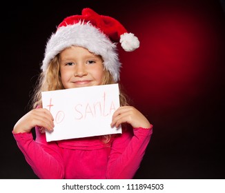 Child With Letter To Santa Claus. Little Girl In Christmas Hat On Black Background