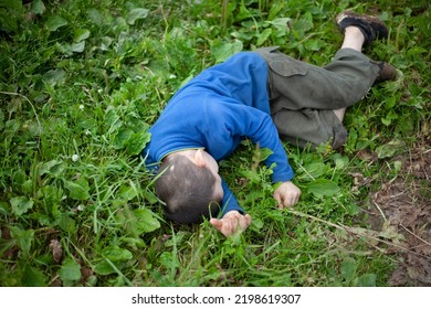 Child lies in grass. Boy fell to ground. Preschooler does not obey and argues. Child is in nature in summer and is dressed in blue jacket and shorts. Child lies without breathing.