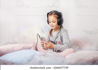 The Child Is Listening To An Audiobook On The Bed. The Concept Of Life, Upbringing, Learning, Music, Childhood.