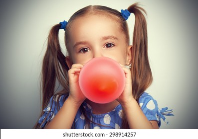 child little girl in a blue dress inflates a red balloon