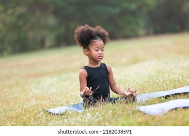 Child Little Girl Doing Meditate Yoga Asana On Roll Mat With Eyes Closed In Park. Kids Girl Practicing Doing Yoga Outdoor