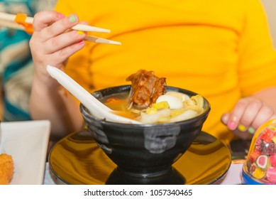 A Child, A Little Girl Is Eating Soup In A Japanese Restaurant.