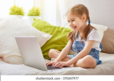 Child little girl with a laptop computer at home. Happy little child plays indoors using pc.