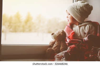 Child Little Girl Sitting By The Window With A Teddy Bear And Looking At The Winter Forest