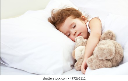 child little girl sleeps in the bed with a toy teddy bear - Powered by Shutterstock