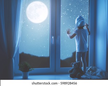 child little girl at the window dreaming the starry sky at bedtime night