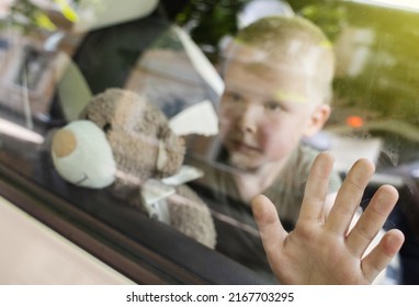 Child locked in car. Blond boy is closed in auto without water. He is hot and his face is red. Irresponsible parents left the child alone in a hot car. Concept of poor care for kids. - Shutterstock ID 2167703295