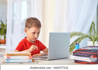 child is looking for information on the Internet through a laptop. self-study at home, doing homework. Intently reading the information on the Internet. boy sits at a table with books and a computer - Powered by Shutterstock