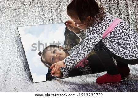 The child is looking in the mirror. Reflection in the mirror of a small child close-up. The blue expanse of the sky is reflected in the mirror.