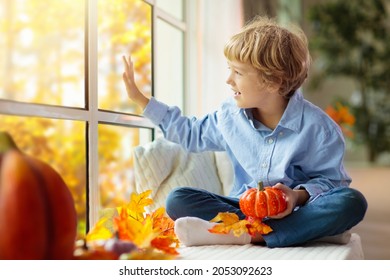 Child Looking Out Of The Window. Autumn Cozy Family Home Decoration. Kids At Home In Fall Watching Golden Leaves In Sunny Garden. Little Boy With Pumpkin On Thanksgiving Day Or Halloween.