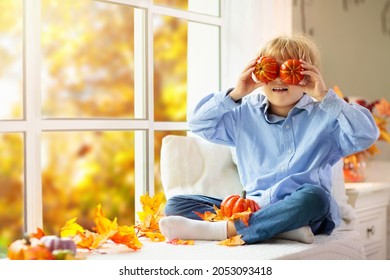 Child Looking Out Of The Window. Autumn Cozy Family Home Decoration. Kids At Home In Fall Watching Golden Leaves In Sunny Garden. Little Boy With Pumpkin On Thanksgiving Day Or Halloween.