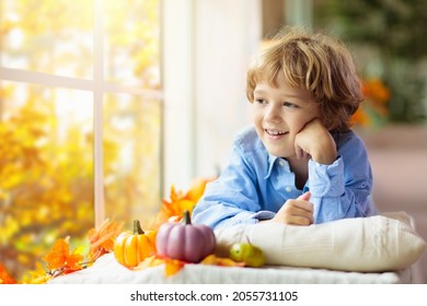 Child Looking Out Of The Window. Autumn Cozy Family Home Decoration. Kids At Home In Fall Watching Golden Leaves In Sunny Garden. Little Boy With Pumpkin On Thanksgiving Day Or Halloween.