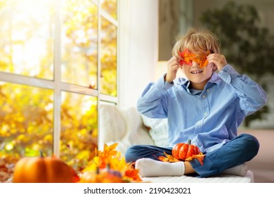 Child Looking Out Of The Window. Autumn Cozy Family Home Decoration. Kids At Home In Fall Watching Golden Leaves In Sunny Garden. Little Boy With Pumpkin On Thanksgiving Day Or Halloween.