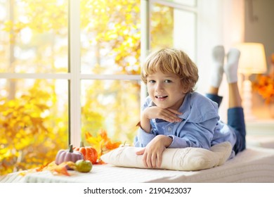 Child Looking Out Of The Window. Autumn Cozy Family Home Decoration. Kids At Home In Fall Watching Golden Leaves In Sunny Garden. Little Boy With Pumpkin On Thanksgiving Day Or Halloween.