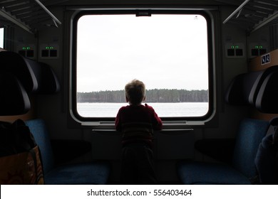 A Child Looking Out The Window Towards The Landscape During A Train Journey. Outside, It Is Snow And Cold Winter.