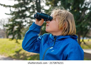 Child Looking Through Binoculars In The Park. Portrait Of A Little Boy Exploring Wildlife. Bird Watching, Hiking, And Adventure Concept.