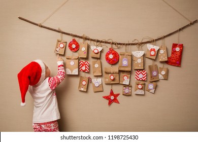 child looks at the advent calendar. Baby girl in a Christmas hat and pajamas shows on first gift.