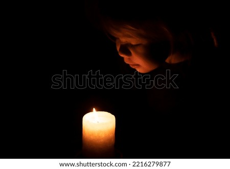 A child looks fascinated from above at the burning flame of a candle in a dark room. Cute girl blowing out the candle. light in darkness