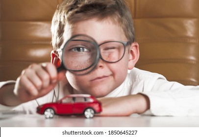 Child Looks On Car With Magnifying Glass. Little Businessman Choose A Car. Kid Boy With Toy Car On His Table