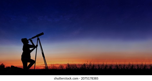 The child looks at the stars through a telescope. A teenager boy looks at the night sky through a spyglass against the backdrop of a sunset while in the field. - Shutterstock ID 2075178385