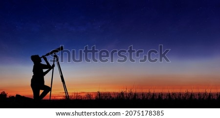 The child looks at the stars through a telescope. A teenager boy looks at the night sky through a spyglass against the backdrop of a sunset while in the field.