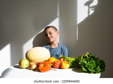 A Child Loves Vegetables, A Boy With A Satisfied Face Sits Near Fresh Vegetables And Fruits