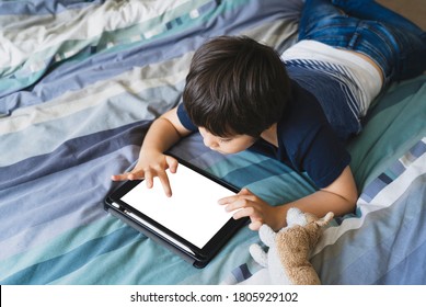 Child lying in bed playing game on digital touch pad in bed room,Young boy lying down with mock up tablet.Home schooling, Social Distance,E-learning online education