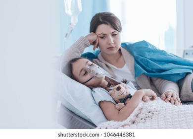 Child Lying In The Hospital In An Oxygen Mask And Her Mother Looking At Her