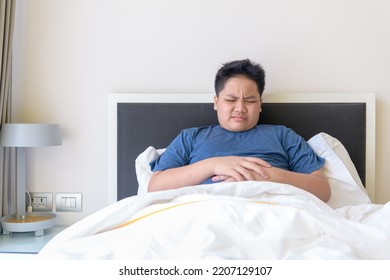 Child Lying On Bed In The Living Room With Stomach Pain. Hands On Belly. Obese Boy Suffering