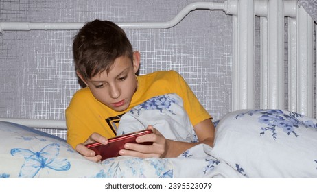 the child is lying on the bed and playing games on a smartphone . - Shutterstock ID 2395523079