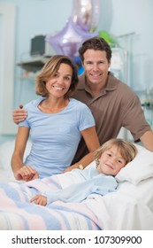 Child Lying On A Medical Bed Next To His Parents In Hospital Ward