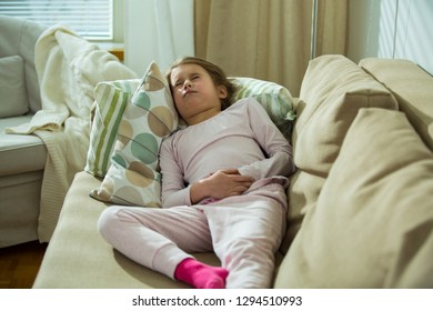 Child Lying On Sofa In The Living Room With Stomach Pain. Hands On Belly. Little Girl Suffering