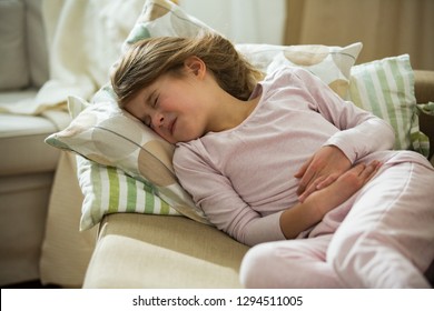 Child Lying On Sofa In The Living Room With Stomach Pain. Hands On Belly. Little Girl Suffering