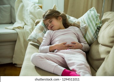 Child Lying On Sofa In The Living Room With Stomach Pain. Hands On Belly. Little Girl Suffering