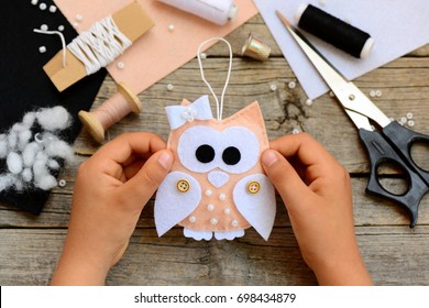 Child made Christmas tree decoration out of felt. Child holds a Christmas tree ornament owl in his hands. Kids workplace concept. Sewing tools and materials on a wooden table. Closeup