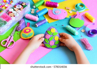 Child made a felt Easter egg ornament. Small child holds a felt Easter egg ornament in his hands. Easter crafts, craft tools and materials on a table. Festive spring crafts concept  - Powered by Shutterstock