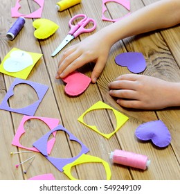 Child Made Hearts Out Of Felt. Children's Hands On The Table. Handmade Valentines Day Heart Gifts, Crafts Materials And Tools On A Wooden Table. Valentine's Day Craft Project