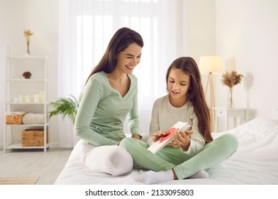 Child Makes Beautiful Surprise For Mom On Mother's Day. Happy Young Caucasian Woman Gets DIY Gift From Her Daughter. Little Girl Sitting On Bed With Mommy And Showing Greeting Card She Made Herself