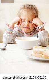 the child makes a face refusing to eat food. The little girl looks at the bowl of soup with disgust. Problems with nutrition