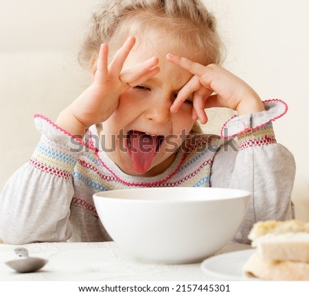 the child makes a face refusing to eat food. The little girl looks at the bowl of soup with disgust. Problems with nutrition