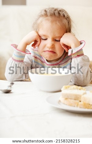 the child makes a face refusing to eat food. The little girl looks at the bowl of soup with disgust. Problems with nutrition