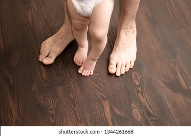 The child makes the first step. Large male legs with small baby legs. Dad helps the child take the first steps. - Shutterstock ID 1344261668