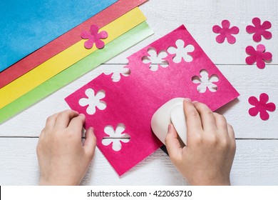 The Child Makes Special Hole Punch Flowers Of Pink Paper. Sheets Of Paper And Cut Out Flowers On White Wooden Table