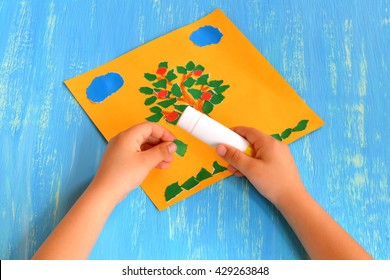 Child makes torn paper tree  Child holds in his hands green paper piece   sticks it  Summer tree paper craft  Idea for preschoolers  Home apple tree applique  Step  by  step  Blue wood background 
