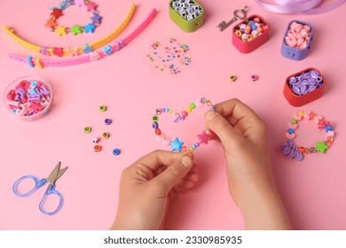 Child making beaded jewelry and different supplies on pink background, above view. Handmade accessories