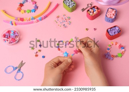 Child making beaded jewelry and different supplies on pink background, above view. Handmade accessories
