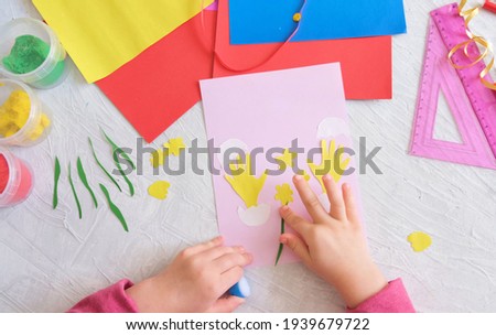 Child making card with Easter funny eggs and flowers  from colorful paper. Handmade. Project of children's creativity, handicrafts, crafts for kids. 
