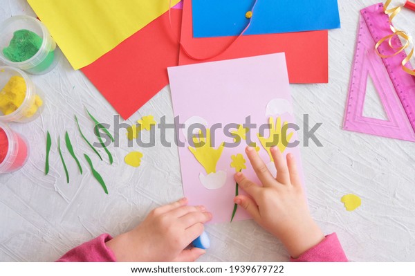 Child making card with Easter funny
eggs and flowers  from colorful paper. Handmade. Project of
children's creativity, handicrafts, crafts for kids.

